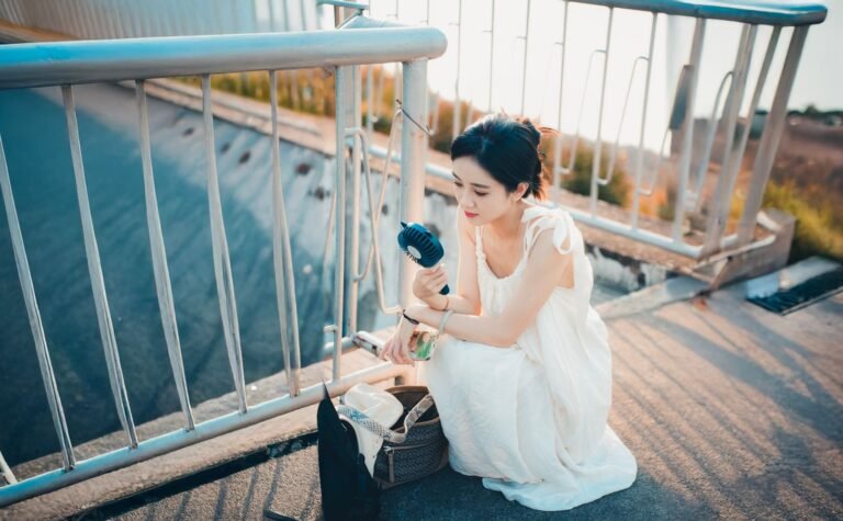 Woman cooling down with a portable handheld fan outdoors on a sunny summer day
