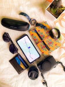 Flat lay of summer travel essentials including smartphone, camera and sunglasses